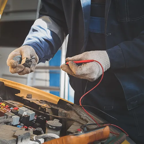 Automotive technician performing electrical diagnostics on a car fuse box using a digital multimeter.