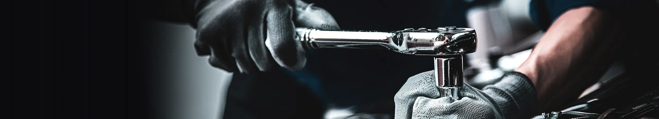 Professional mechanic wearing protective gloves using a socket wrench for car maintenance.