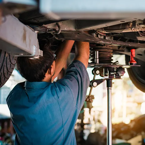 Auto repair technician working under a vehicle on a lift using a supportive jack.