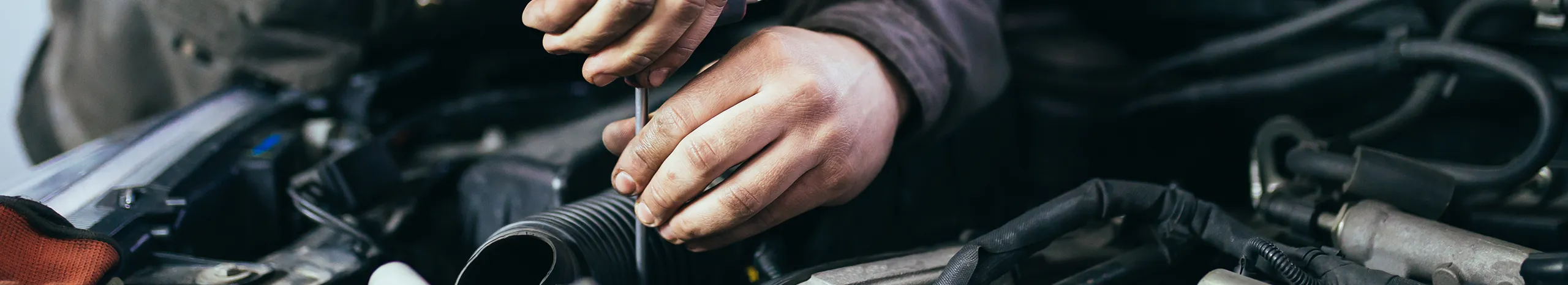 Close-up of a mechanic's hands using a screwdriver to repair automotive engine parts.