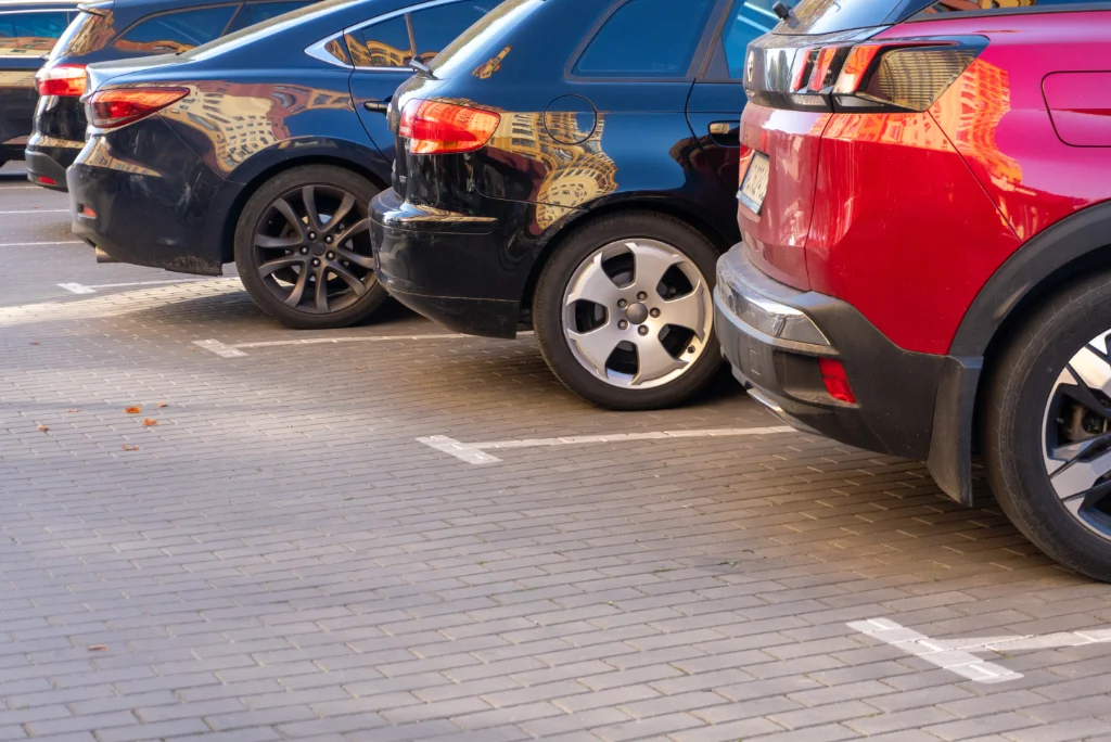 A row of modern cars parked backwards in designated parking spaces on a paved cobblestone lot, showing their rear profiles and wheels.